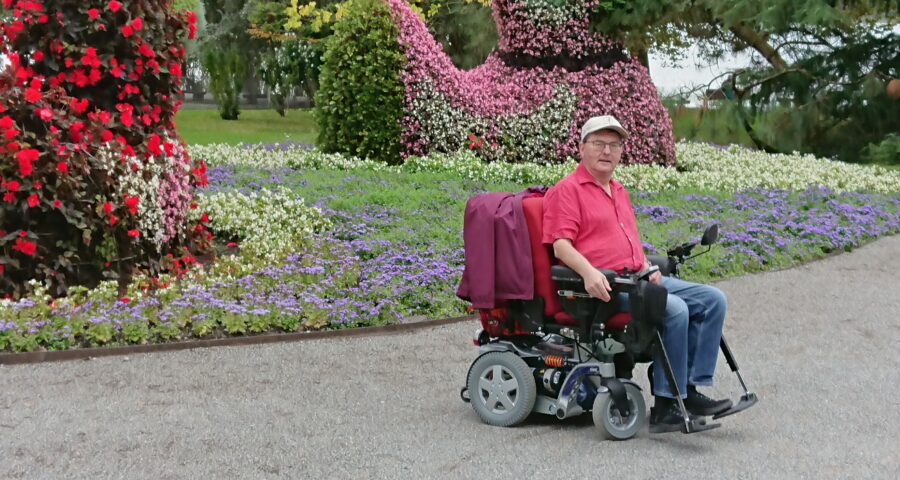 Norbert Sandmann sitzt in seinem Elektrorollstuhl vor einer Blumenkulisse auf der Insel Mainau.
